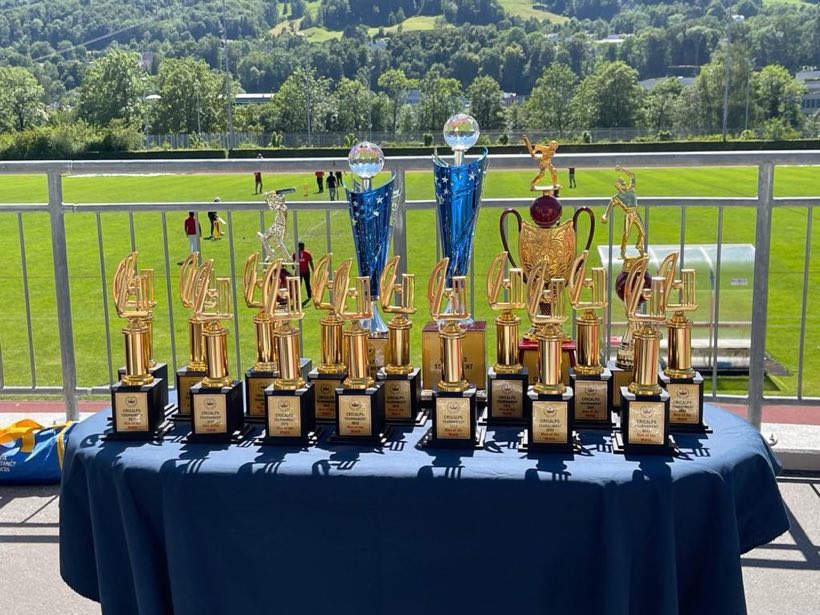 A long table of tournament trophies set out on a balcony above a green playing field