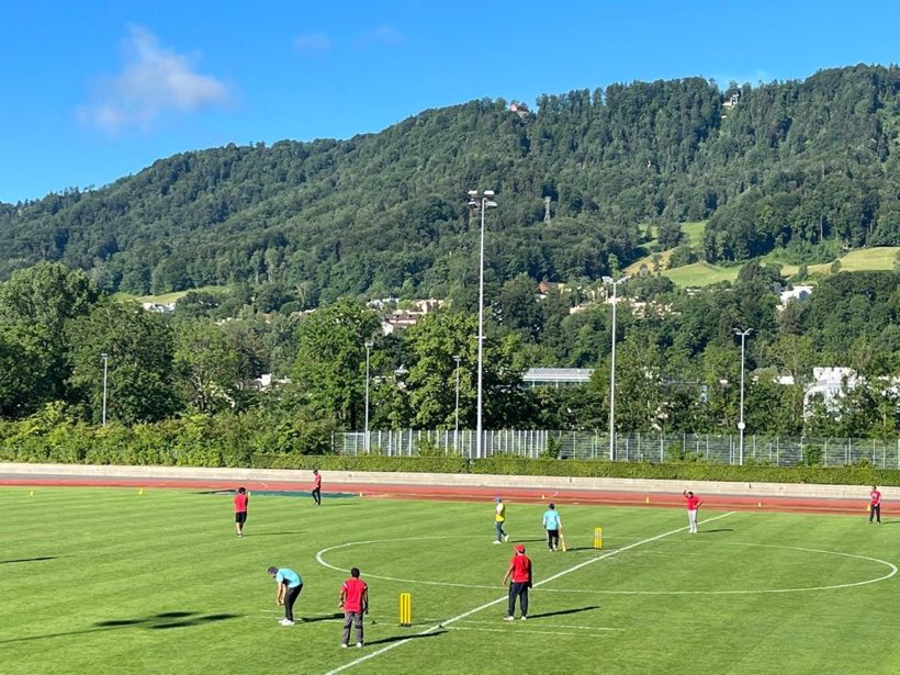 The green ground under a blue sky with a wooded hill rising behind it