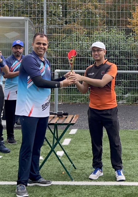 Two captains shaking hands and exchanging an award on the artificial turf