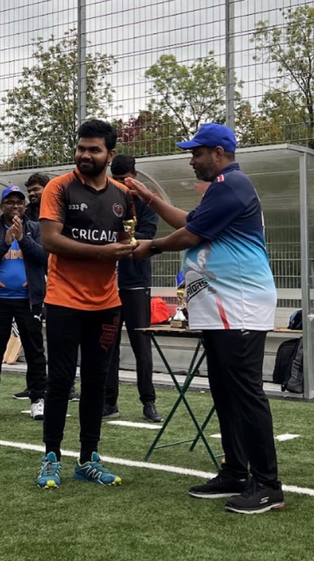 A trophy handed over between two players on the artificial pitch